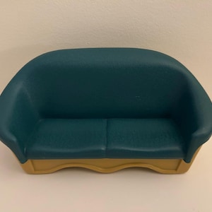 May include: A small teal sofa with a curved back and a two-cushion seat. The base of the sofa is a light tan colour. The sofa is a toy or decorative item.