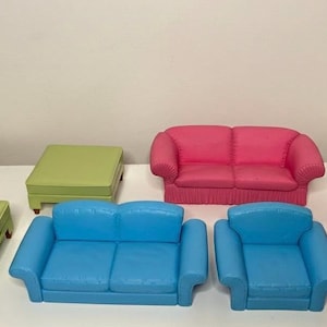 May include: A selection of miniature furniture in different colours. Includes a green armchair, a green ottoman, a pink loveseat, a blue loveseat, a blue armchair, and a pink armchair. The furniture is made of a smooth material.
