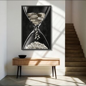 May include: A rectangular wall art print featuring a black and white hourglass. The top bulb contains stacks of US dollar bills, while individual bills fall through the centre neck into a large pile of currency accumulating in the bottom bulb.