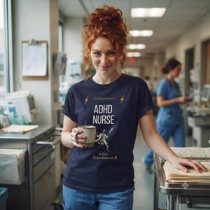 May include: A navy blue t-shirt featuring the text "NEURODIVERGENT", "ADHD NURSE", and "Wildly Hyperfocused" with lightning bolt icons and a graphic of a person in a lab coat. The shirt is worn with blue scrub pants and a plain ceramic mug.