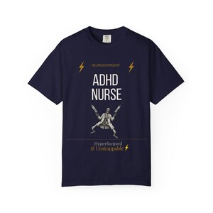 Op de afbeelding: Een marineblauw t-shirt met korte mouwen en de tekst NEURODIVERGENT, ADHD NURSE en Hyperfocused & Unstoppable. Het ontwerp bevat twee gele bliksemschichten en een afbeelding van een skelet in een doktersjas met twee injectiespuiten.