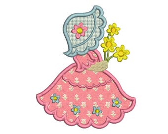 Può includere: Un colorato disegno ricamato di una ragazza con un cappello che tiene in mano un mazzo di fiori gialli. L'abito rosa della ragazza ha un motivo floreale e il cappello è azzurro con un motivo a scacchi. Il disegno è bordato di rosa.