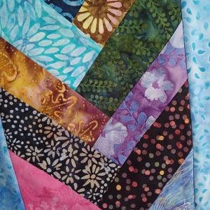 May include: Close-up of a patchwork textile with a chevron design. The fabric features various patterns and colors, including blue swirls, floral prints in brown and white, and pink and purple hues. The design is a mix of textures and colors.