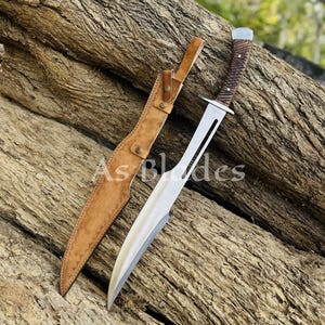 May include: A large, silver blade knife with a brown wooden handle and a tan leather sheath. The knife is lying on a weathered wooden surface. The text "As Blades" is visible on the image.