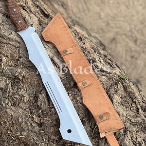 May include: A large, silver blade with a brown wooden handle and a leather sheath. The blade has a unique shape with a pointed tip and several grooves. The sheath is tan and has decorative stitching and button closures. The text "As Blades" is visible.