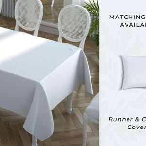 Puede incluir: Un mantel blanco cubre una mesa de comedor, con sillas blancas a juego. Un jarrón con flores amarillas está sobre la mesa. También se ve el texto "MATCHING ITEMS AVAILABLE" y "RUNNER & CUSHION COVERS".