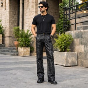 May include: A black short-sleeved t-shirt paired with black trousers featuring a textured crocodile-skin pattern. The outfit includes a silver chain necklace, a wristwatch, and black sunglasses. The trousers have a straight-leg cut.