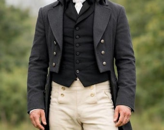 Puede incluir: Un conjunto de vestuario histórico con un abrigo gris oscuro, chaleco negro y calzones color crema. El atuendo incluye una corbata blanca y botas negras hasta la rodilla. El abrigo tiene botones decorativos. La persona está de pie en un campo de hierba.
