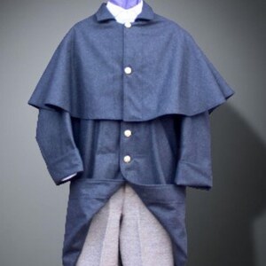 Può includere: Un cappotto blu navy in stile vintage con uno strato superiore a forma di mantello e tre bottoni color oro. Il cappotto è abbinato a pantaloni grigio chiaro, una camicia bianca con colletto e una cravatta viola.