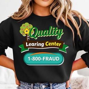 Peut inclure: Sweat-shirt noir avec un motif graphique. Le motif comprend les mots "Quality Learning Center" en vert et jaune, une illustration de cabane dans les arbres et le numéro de téléphone 1-800-FRAUD dans un ovale turquoise.