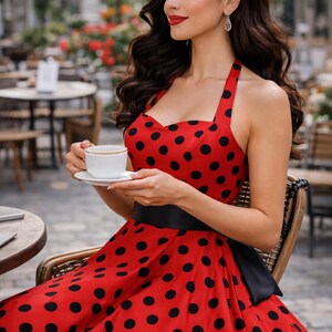 K&ouml;nnte beinhalten: Ein rotes Kleid mit schwarzen Punkten und einem schwarzen G&uuml;rtel. Das Kleid wird von einer Person getragen, die eine wei&szlig;e Tasse und Untertasse h&auml;lt. Die Person sitzt in einem Stuhl in einem Stra&szlig;encaf&eacute;.
