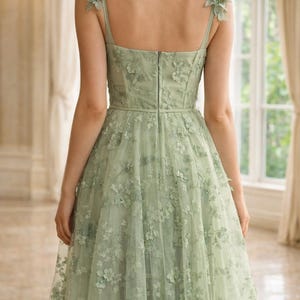 Puede incluir: Vestido formal verde claro con adornos florales. El vestido presenta un corpi&ntilde;o ajustado, una falda amplia y delicados detalles florales en los hombros y en toda la capa de tul. El vestido tiene cierre de cremallera en la espalda.