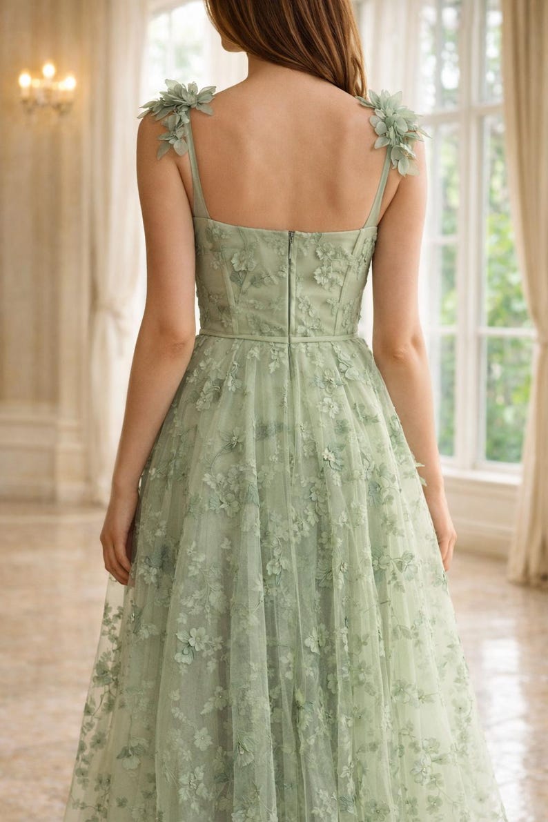 Puede incluir: Vestido formal verde claro con adornos florales. El vestido presenta un corpi&ntilde;o ajustado, una falda amplia y delicados detalles florales en los hombros y en toda la capa de tul. El vestido tiene cierre de cremallera en la espalda.