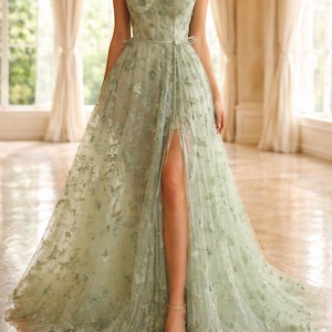 Puede incluir: Vestido largo verde claro con bordados florales y una abertura alta. El vestido presenta un escote coraz&oacute;n, adornos florales en los hombros y una falda fluida. La modelo lleva sandalias doradas. Adecuado para eventos formales.