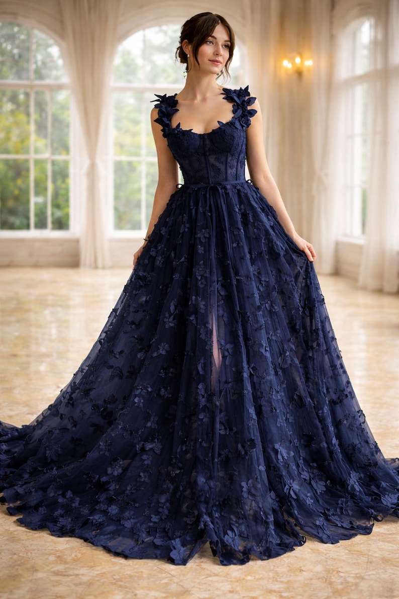 Puede incluir: Un vestido de noche azul marino con adornos florales. El vestido presenta un corpi&ntilde;o ajustado, una falda fluida y delicados detalles florales en los hombros y en la falda. El vestido tiene una abertura alta y una larga cola.