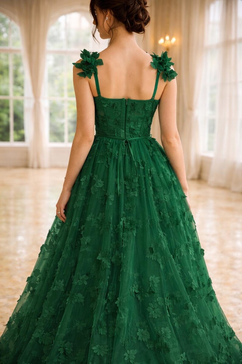 Puede incluir: Vestido de noche verde esmeralda con adornos florales. El vestido presenta un corpi&ntilde;o ajustado, tirantes delicados y una falda de tul fluida adornada con aplicaciones florales en 3D. La espalda tiene cierre de cremallera y lazo.