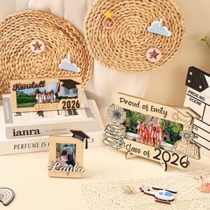 May include: Wooden photo frames with graduation themes. One frame reads "Kendall Class of 2026", another says "Proud of Emily Class of 2026", and a third says "Layla". Decorative wooden cutouts of a graduation cap, clouds, stars, and a helicopter are also present.