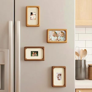 May include: Four wooden magnetic picture frames of varying sizes are displayed on a refrigerator. Each frame holds a photograph. The frames have a light wood finish and a cream-coloured matting around the photos. The photos appear to be family portraits.