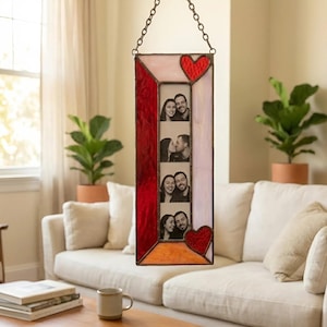 May include: A hanging stained glass photo frame with a red, pink, and orange design. The frame holds four black and white photos and features two red heart accents. It hangs from a metal chain.