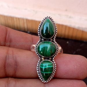May include: A silver ring featuring three vertically aligned malachite stones. The centre stone is oval-shaped, while the top and bottom stones are teardrop-shaped. The stones are set in a twisted rope-style silver metal frame with a polished finish.