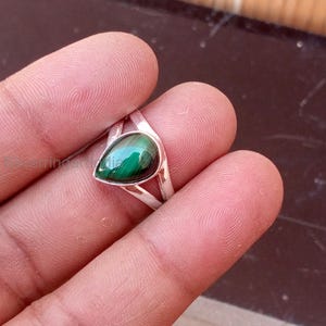 Może przedstawiać: Srebrny pierścionek z malachitem w kształcie łzy. Malachit ma głęboki zielony kolor z ciemniejszymi zielonymi żyłkami. Pierścionek ma prosty, elegancki design.