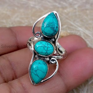 May include: A silver ring featuring three turquoise stones. The stones are oval and teardrop-shaped, set in a decorative silver band. The turquoise stones have a distinctive blue-green color with dark veining.