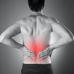 Puede incluir: Imagen en escala de grises de la espalda de una persona, con un área roja que indica dolor en la zona lumbar. La persona está sin camisa, usa pantalones cortos de color gris oscuro y tiene las manos en la zona lumbar.