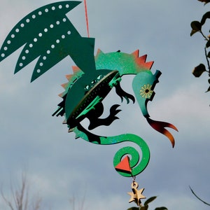May include: A green, red and gold metal mobile with a dragon design. The mobile has a spiral tail, a star at the bottom, and a triangle shape hanging from the tail.