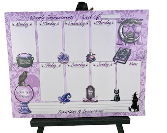 May include: A purple weekly planner with the text "Weekly Enchantments" and "Intentions & Incantations." It features illustrations of a cauldron, crystal, books, a cat, a witch, and a crescent moon with a chair. The planner is on a black easel.