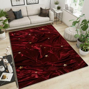 Könnte beinhalten: Ein rechteckiger burgunderfarbener Teppich mit Samtstruktur und goldenen Sternakzenten. Der Teppich liegt auf einem hellen Holzboden in einem Wohnzimmer, mit einem beigen Sofa und Pflanzen im Hintergrund.