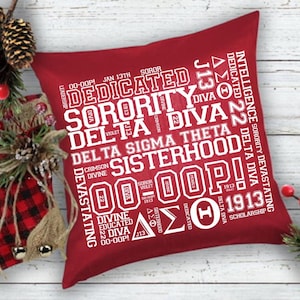 May include: A square, red decorative pillow with white text. The text includes the words "Dedicated," "Sorority," "Delta Diva," and "Sisterhood." Additional text includes "Intelligence," "Devastating," and "Scholarship."