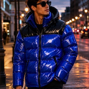 Könnte beinhalten: Eine glänzende, leuchtend blaue Daunenjacke mit einem schwarzen Einsatz über den Schultern und der Brust. Die Jacke verfügt über einen hohen Kragen, eine Kapuze und einen durchgehenden schwarzen Frontreißverschluss. Das Material ist glänzend.