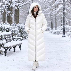 May include: A long, glossy white puffer coat featuring a full-length front zip, a hood, and a chevron-quilted pattern. The coat extends to the lower calf and is worn with light-coloured boots, providing full-body coverage in a snowy environment.