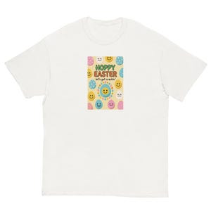 May include: White t-shirt with a colourful graphic featuring the text "HOPPY EASTER" and "let's get crackin'" surrounded by smiling eggs and a sun. The design is in pastel colours, perfect for Easter.