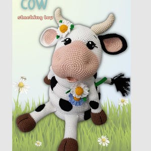 May include: A crocheted cow stacking toy with a white body, black spots, and brown hooves. The cow has a pink nose, black eyes, and a daisy flower crown. The text "COW stacking toy" is at the top of the image.