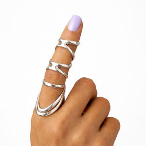 Può includere: Un set di anelli da dito in argento. Il set comprende un anello grande alla base del dito, tre anelli al centro del dito e due anelli sulla parte superiore del dito. Gli anelli sono in metallo argentato lucido.