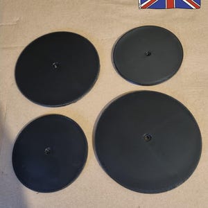May include: Four black, circular objects with a central hole are displayed on a brown surface. The text "Made in the UK" is visible, along with a Union Jack flag.