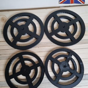 May include: Four black circular coasters with a geometric design. Each coaster has a central hole and radiating spokes, creating an open, symmetrical pattern. The text "Made in the UK" is visible.