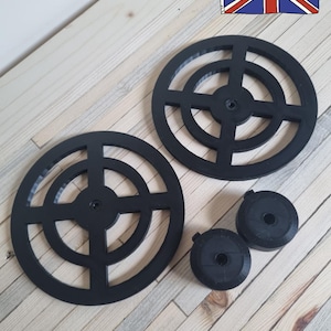 May include: Black circular components with a cross-shaped design and smaller, round pieces. The text "Made in the UK" is displayed, accompanied by a Union Jack illustration. The items are set on a light wood-grain surface.