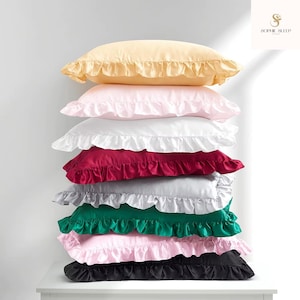 May include: A stack of seven ruffled silk pillowcases in various colors: yellow, pink, white, burgundy, gray, green, and black. The pillowcases are stacked on top of each other, showcasing the different colors and textures.