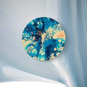 Può includere: Opera d'arte astratta rotonda con un design fluido nei toni del blu, turchese e beige. L'opera presenta una superficie strutturata e una forma rotonda, creando un'estetica moderna e artistica. Diametro di circa 30 cm.