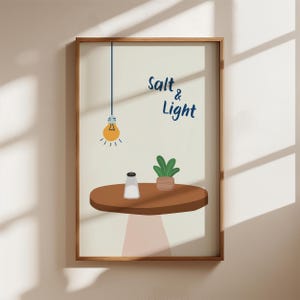 Könnte beinhalten: Ein gerahmter Kunstdruck mit einem braunen Tisch mit einem Salzstreuer und einer kleinen Topfpflanze. Über dem Tisch hängt eine Glühbirne. Die Worte "Salt & Light" sind in blauer Schrift geschrieben. Der Hintergrund ist hellbeige.