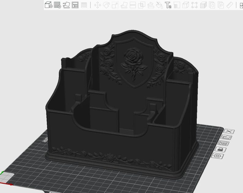 May include: A matte black desktop organizer featuring a central shield-shaped back panel embossed with a detailed rose motif. The structure includes multiple compartments of varying heights for storage, with additional rose vine relief detailing.
