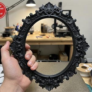 May include: An oval-shaped black picture frame featuring intricate relief carvings of floral motifs and ornate scrollwork along the entire border. The frame has a prominent decorative crest at the top and bottom. Text in the corner reads: Digital Download NOT physical item.