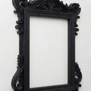 Puede incluir: Marco de fotos negro ornamentado con intrincados detalles de volutas y una abertura rectangular. El marco tiene un diseño gótico con una parte superior y laterales decorativos. El texto en la imagen dice "it's NOT physical item No Shipping".