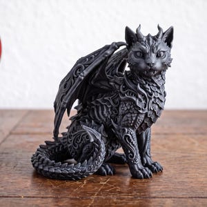 May include: A matte black figurine of a cat with dragon-like features, including wings, horns, and a scaled tail. The surface is covered in intricate, embossed scrollwork patterns. A red circular badge displays the text Digital Download NOT physical item.