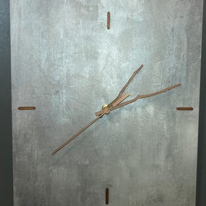 May include: A rectangular wall clock with a textured gray face. The clock features brown wooden hands and hour markers. The hands are designed to resemble tree branches. The clock is a modern home decor item.