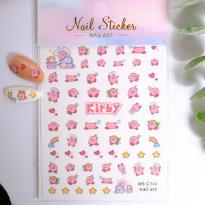 K&ouml;nnte beinhalten: Nagelkunst-Aufkleber mit einem rosa Cartoon-Charakter in verschiedenen Posen, Herzen, Sternen und Regenbogen. Das Blatt enth&auml;lt den Text "Kirby" und "Nail Sticker - Nail Art". Zwei Nagelkunst-Beispiele sind links abgebildet.