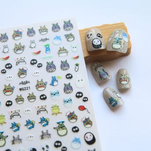 May include: A sheet of nail art stickers with cartoon characters, including Totoro and other designs. The stickers are colourful and detailed, with images of characters, food, and other small objects. The sheet has the text "WG221" printed on it.
