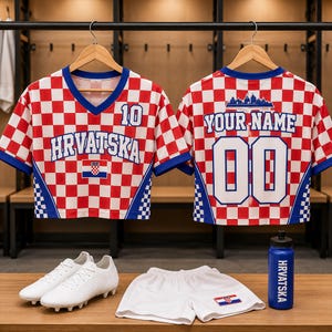 Puede incluir: Dos camisetas de manga corta con patr&oacute;n de cuadros rojos y blancos, bordes azules y el texto HRVATSKA, 10, YOUR NAME y 00. Incluye pantalones cortos blancos con una peque&ntilde;a bandera croata, botas de f&uacute;tbol blancas y una botella azul HRVATSKA.